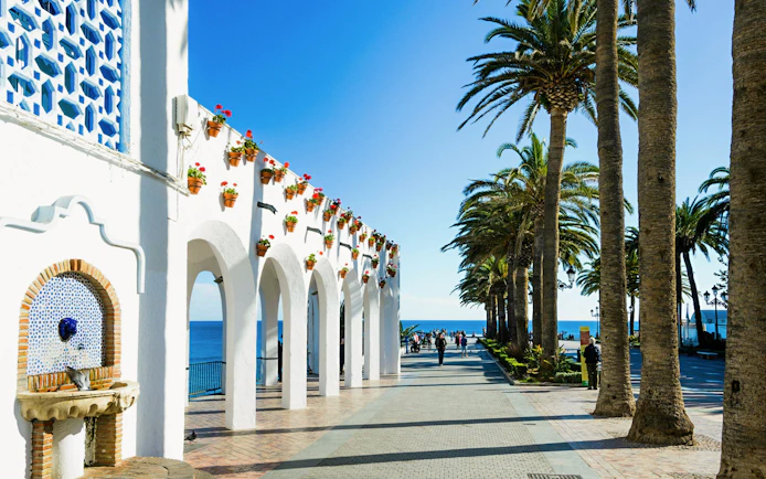 White arches and palm trees along the promenade at Plaza Balcon de Europa, Nerja, Spain.