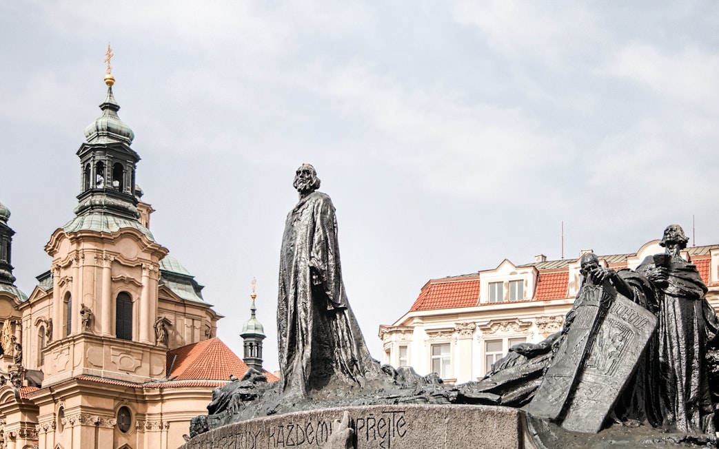 Statue of Jan Hus in Prague's Old Town Square with church in background.