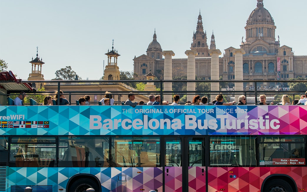 Barcelona Bus Turistic with tourists, Montjuïc Palace in background.
