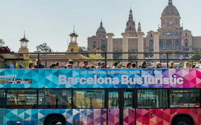 Barcelona Bus Turistic with tourists, Montjuïc Palace in background.