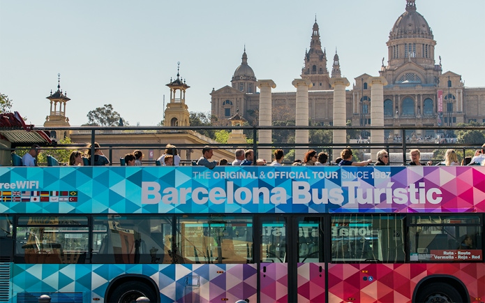 Barcelona Bus Turistic with tourists, Montjuïc Palace in background.