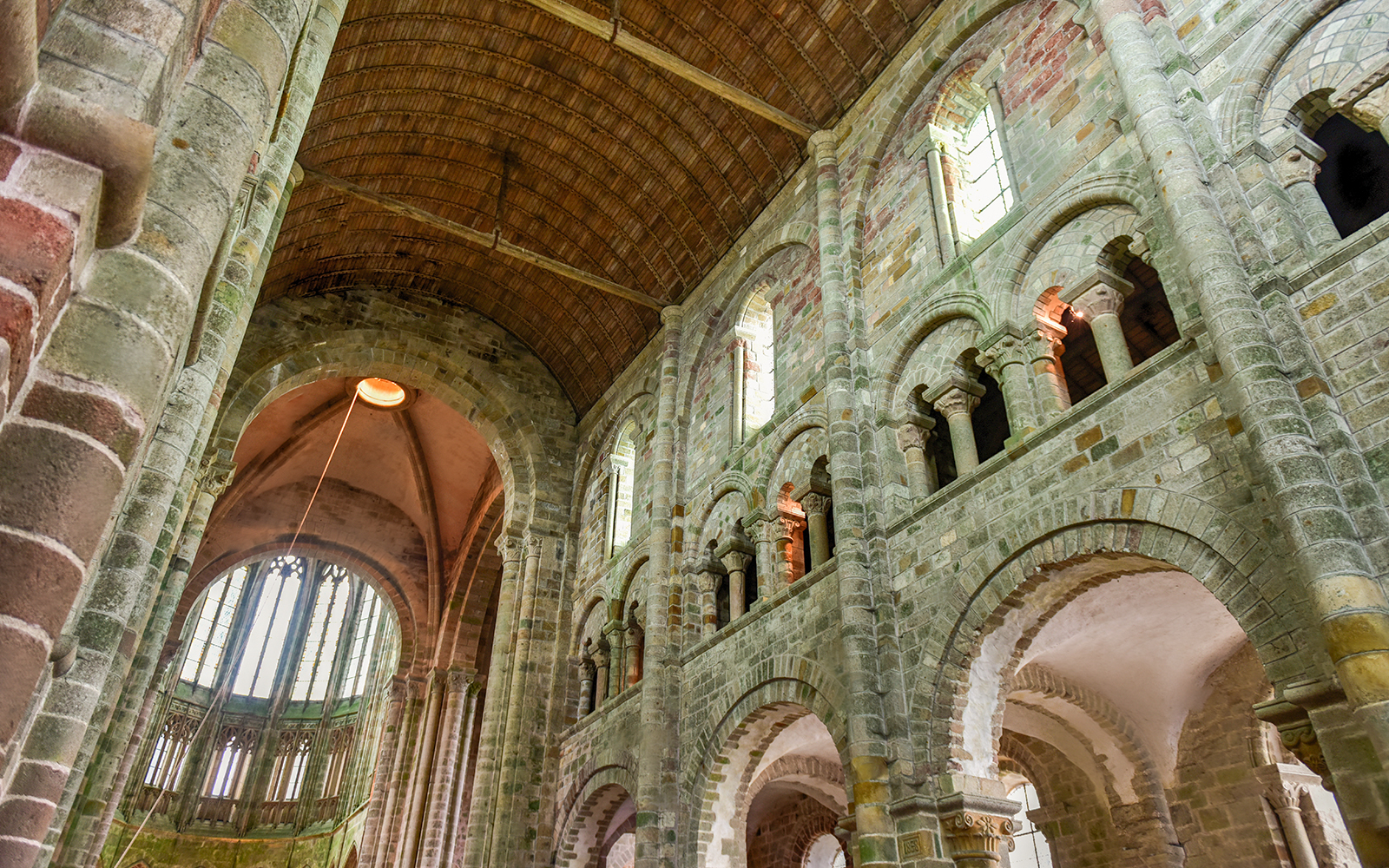 Interior of Mont Saint-Michel Abbey with stone arches and vaulted ceiling, Normandy, France.