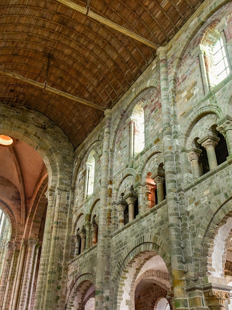 Interior of Mont Saint-Michel Abbey with stone arches and vaulted ceiling, Normandy, France.