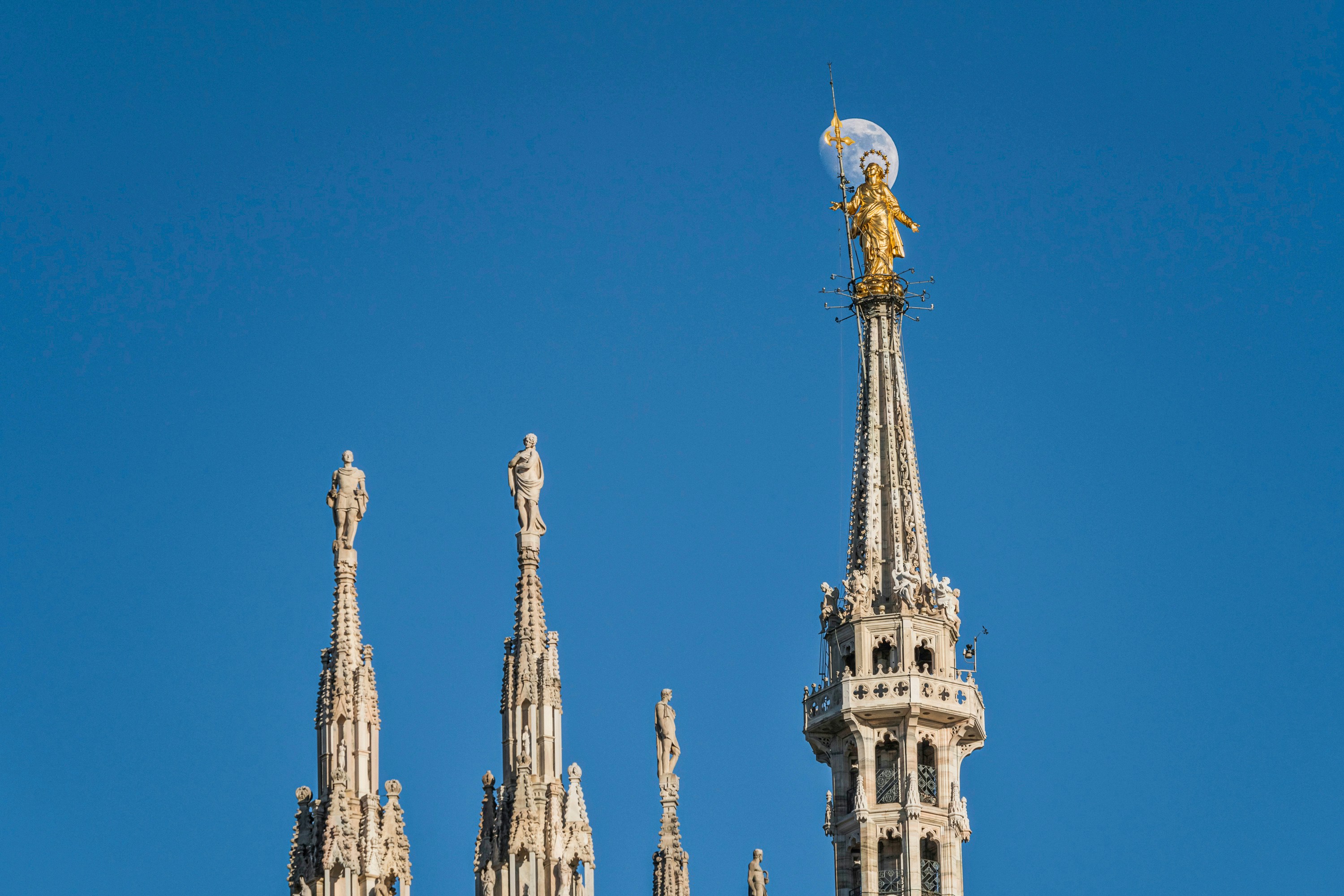 Madonnina Statue atop Milan Cathedral with moon in the background.