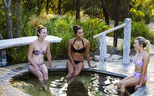 Visitors relaxing in a hot spring pool at Peninsula Hot Springs, surrounded by lush greenery.