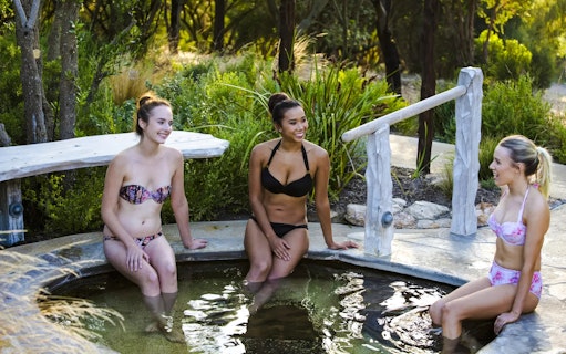 Visitors relaxing in a hot spring pool at Peninsula Hot Springs, surrounded by lush greenery.