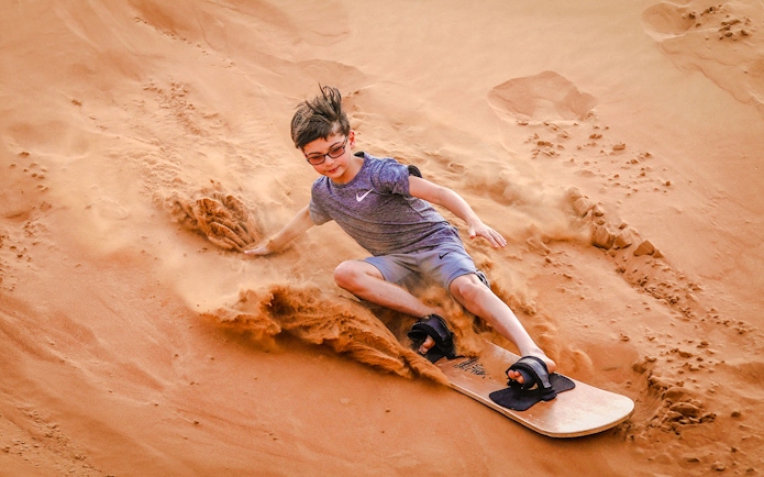 Child sandboarding down a dune during Abu Dhabi desert safari.