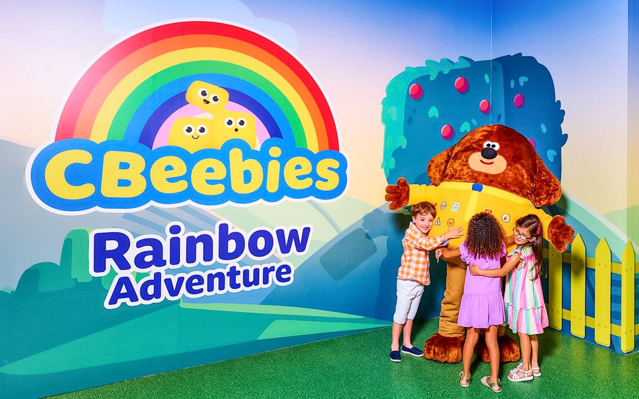 Children hugging a large character at CBeebies Rainbow Adventure.