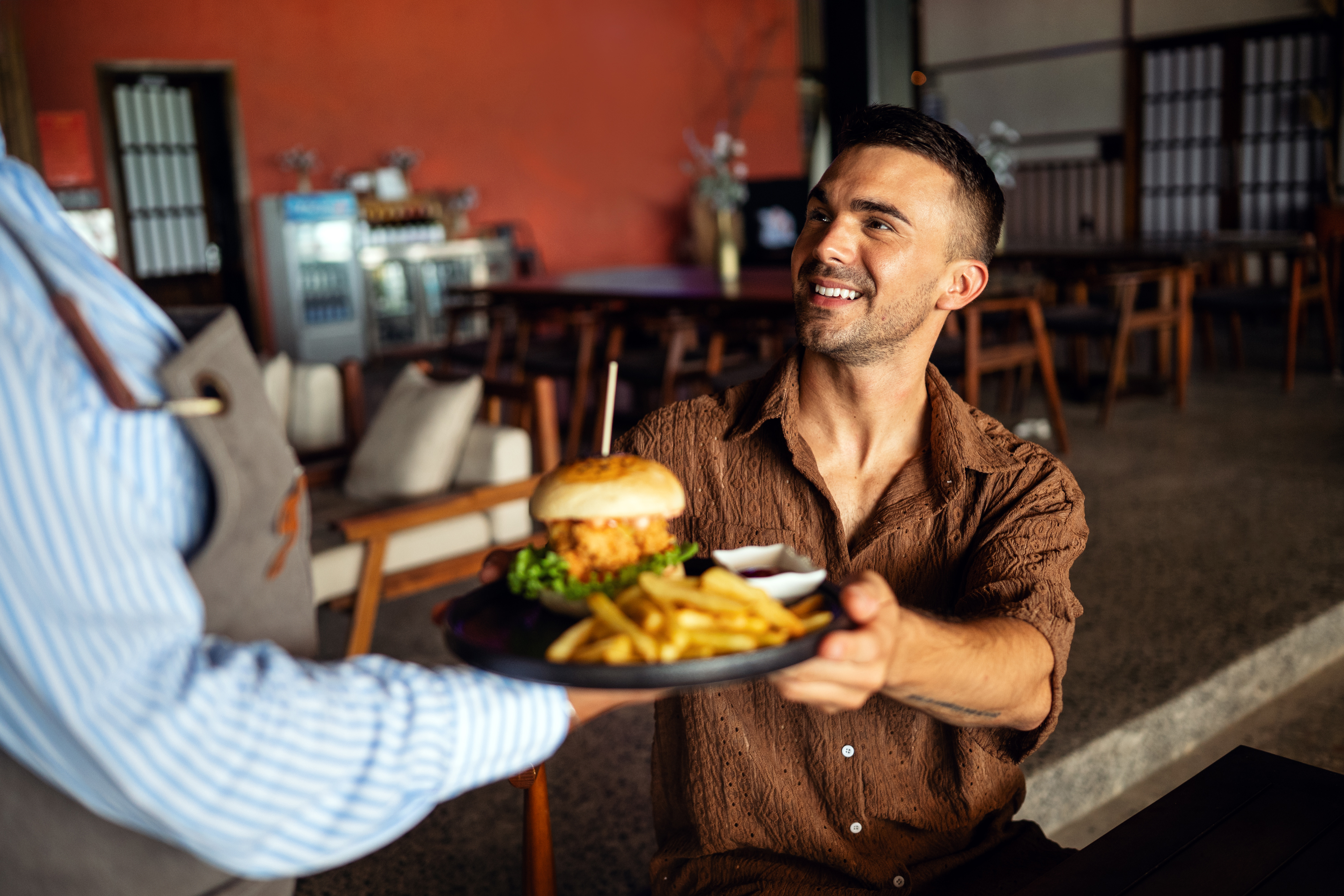 Waitress serves burger and fries to a smiling customer in a restaurant.