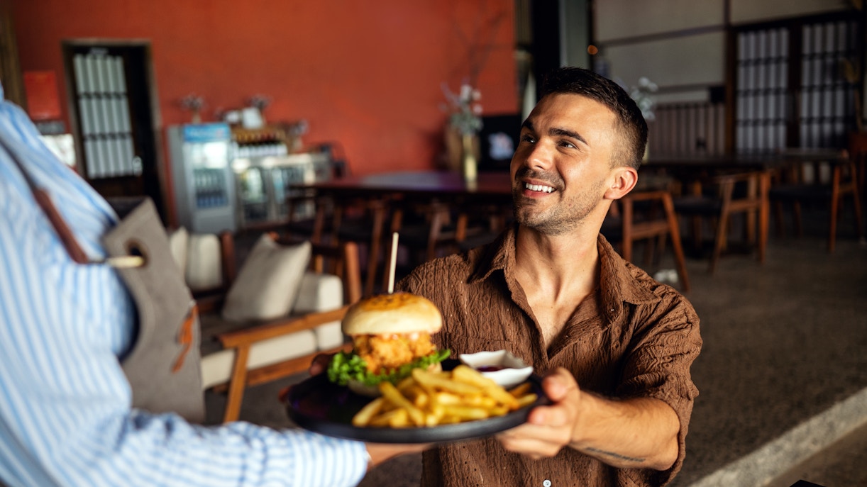 Waitress serves burger and fries to a smiling customer in a restaurant.