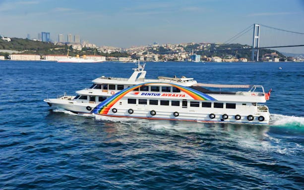 Hop-on hop-off boat cruising on the Bosphorus with Istanbul skyline and bridge in view.
