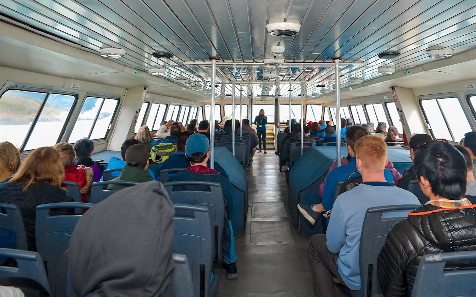 Tourists seated inside Perito Moreno Cruise with guide speaking at front.