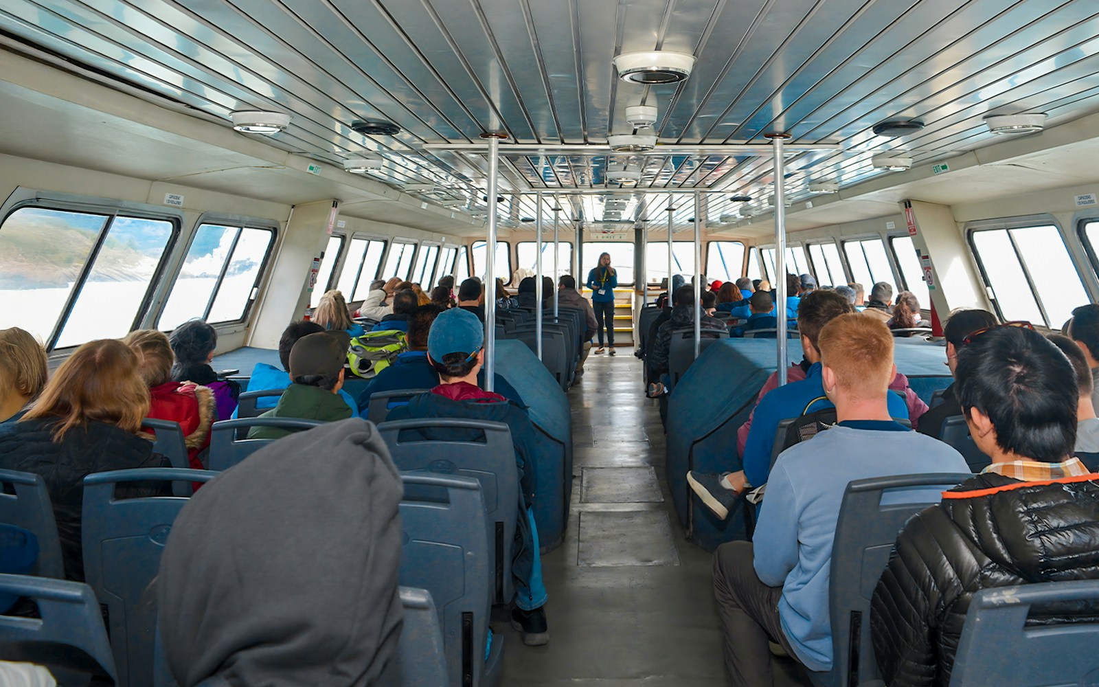 Tourists seated inside Perito Moreno Cruise with guide speaking at front.