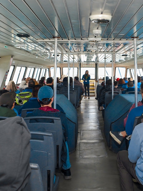 Tourists seated inside Perito Moreno Cruise with guide speaking at front.