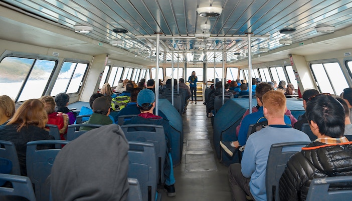 Tourists seated inside Perito Moreno Cruise with guide speaking at front.