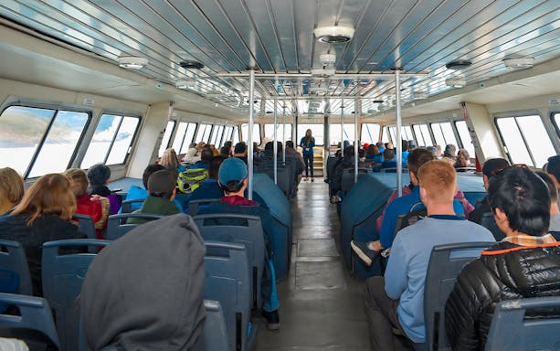 Tourists seated inside Perito Moreno Cruise with guide speaking at front.