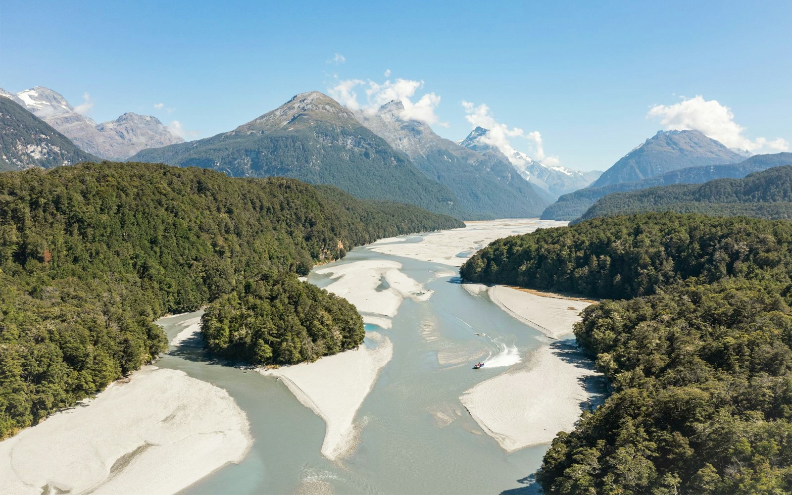 Jet boat navigating Dart River surrounded by lush forests and mountains in New Zealand.