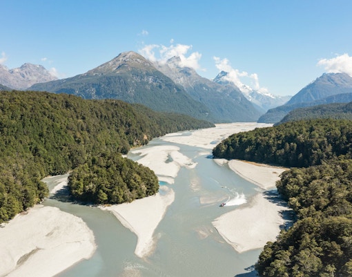 Jet boat navigating Dart River surrounded by lush forests and mountains in New Zealand.