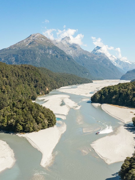 Jet boat navigating Dart River surrounded by lush forests and mountains in New Zealand.