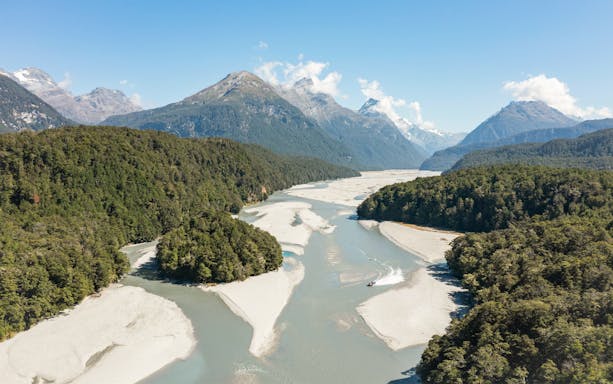 Jet boat navigating Dart River surrounded by lush forests and mountains in New Zealand.