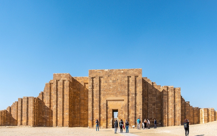 Entrance to the Pyramid of Djoser complex in Saqqara, Egypt, with visitors exploring.