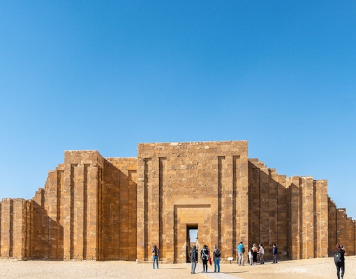 Entrance to the Pyramid of Djoser complex in Saqqara, Egypt, with visitors exploring.