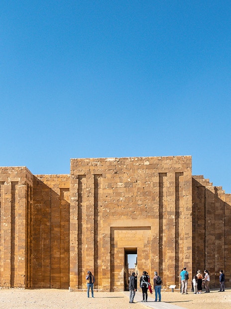 Entrance to the Pyramid of Djoser complex in Saqqara, Egypt, with visitors exploring.