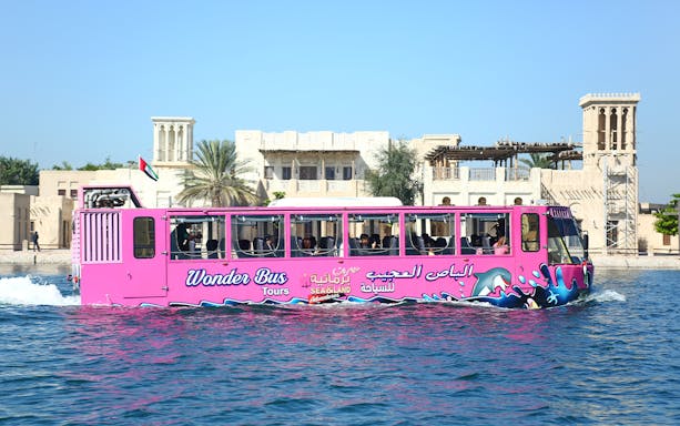 Dubai Wonder Bus on water with traditional buildings in the background.