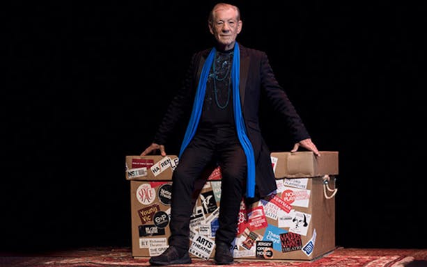 Actor sitting on a prop box covered in theater stickers during Ian McKellen On Stage performance.