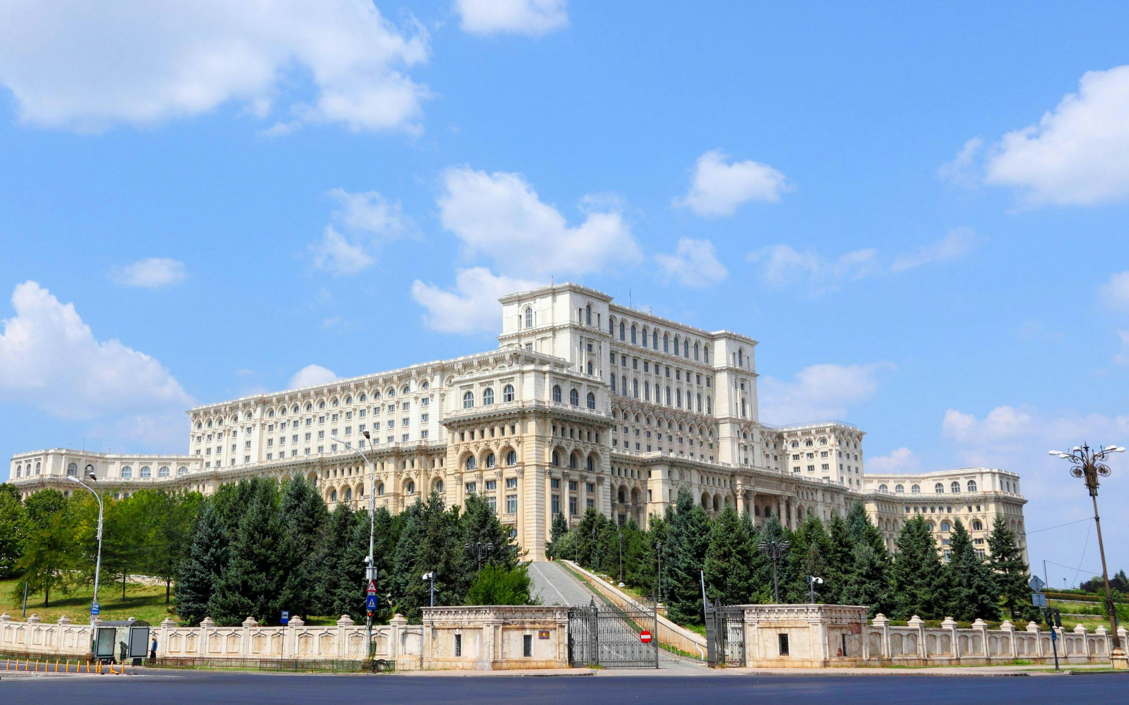 Palace of Parliament in Bucharest, Romania, with surrounding trees and clear sky.