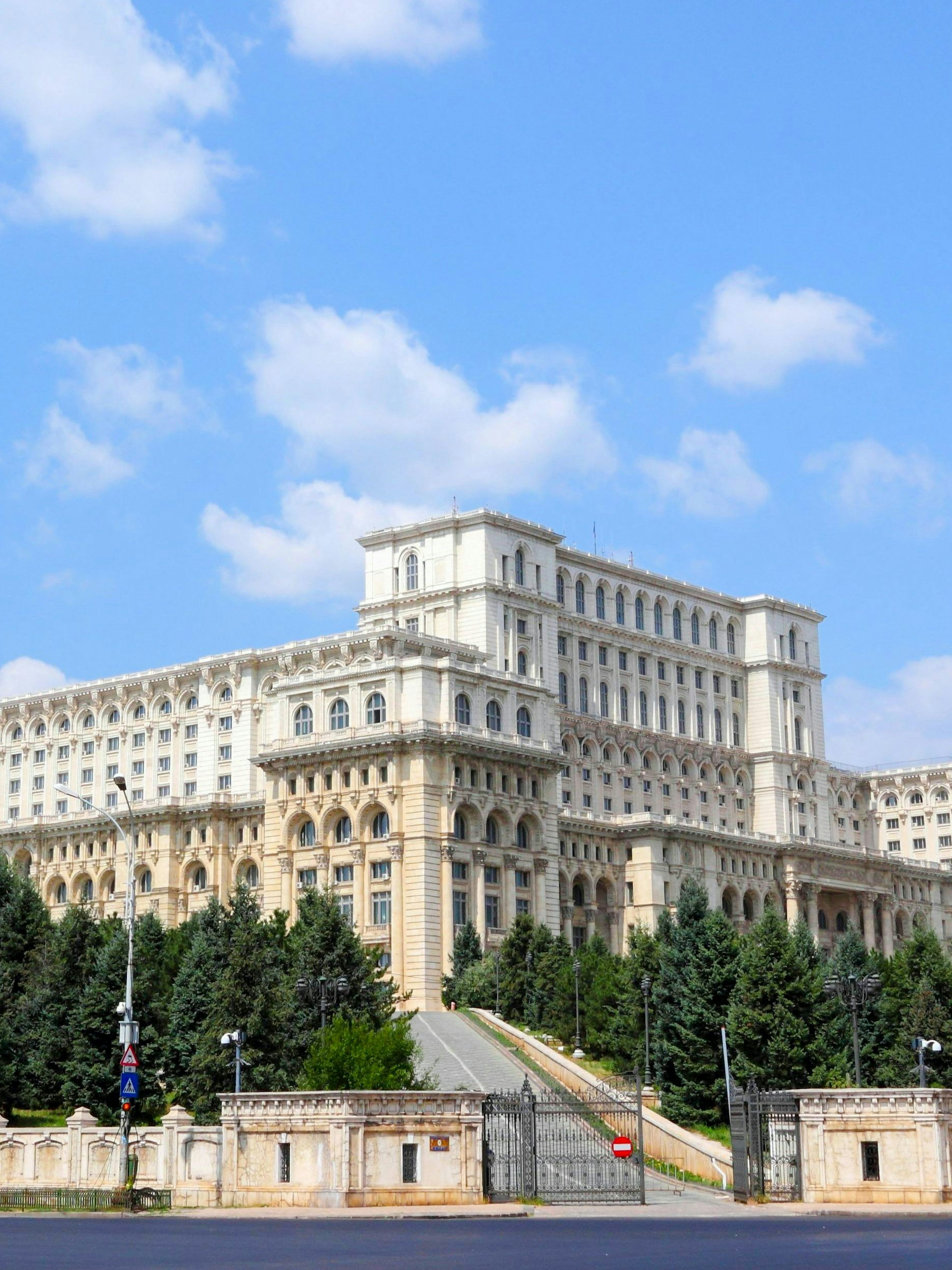 Palace of Parliament in Bucharest, Romania, with surrounding trees and clear sky.