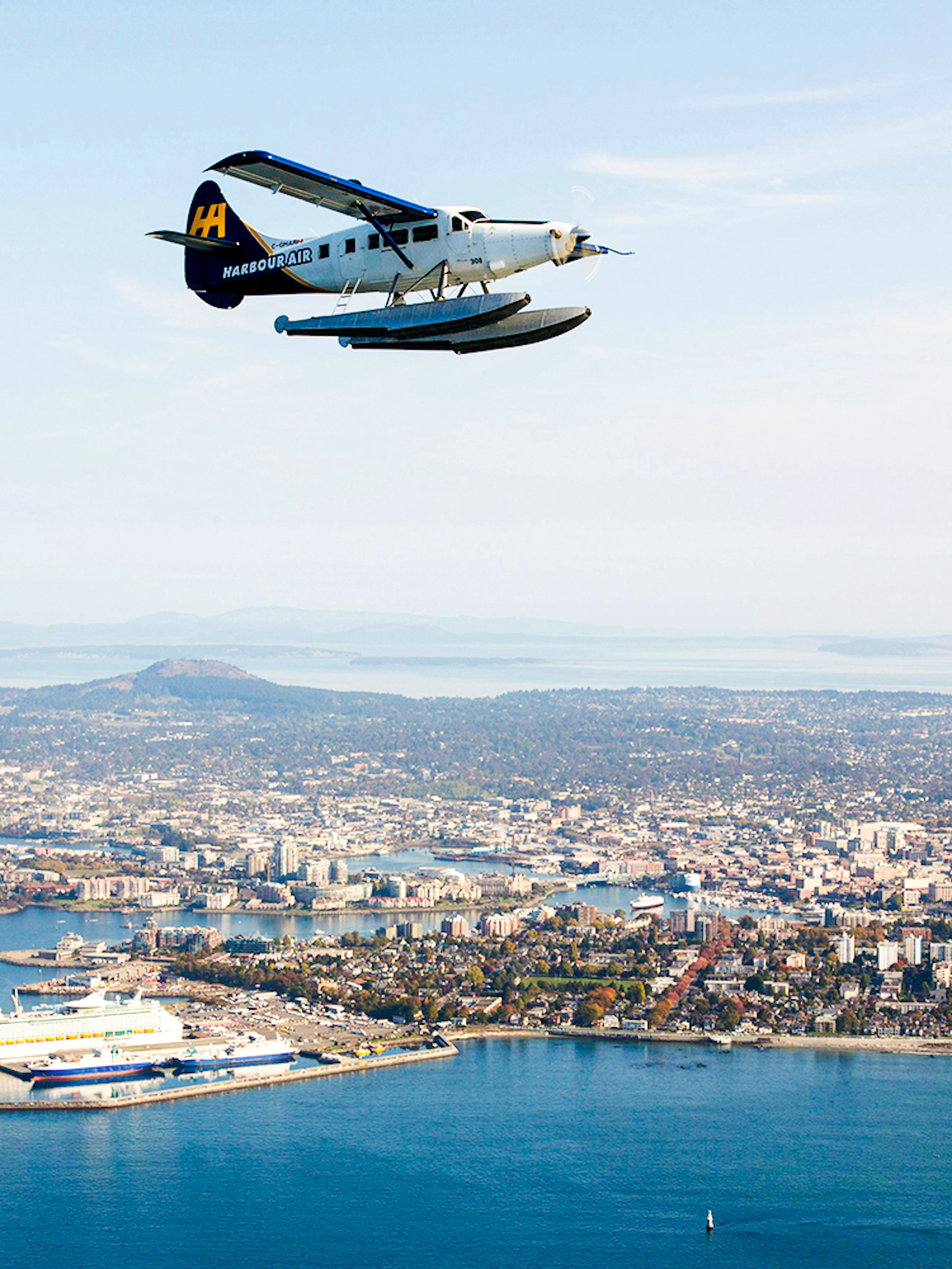 Seaplane flying over Victoria's coastline with cityscape and islands in view.