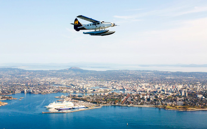 Seaplane flying over Victoria's coastline with cityscape and islands in view.