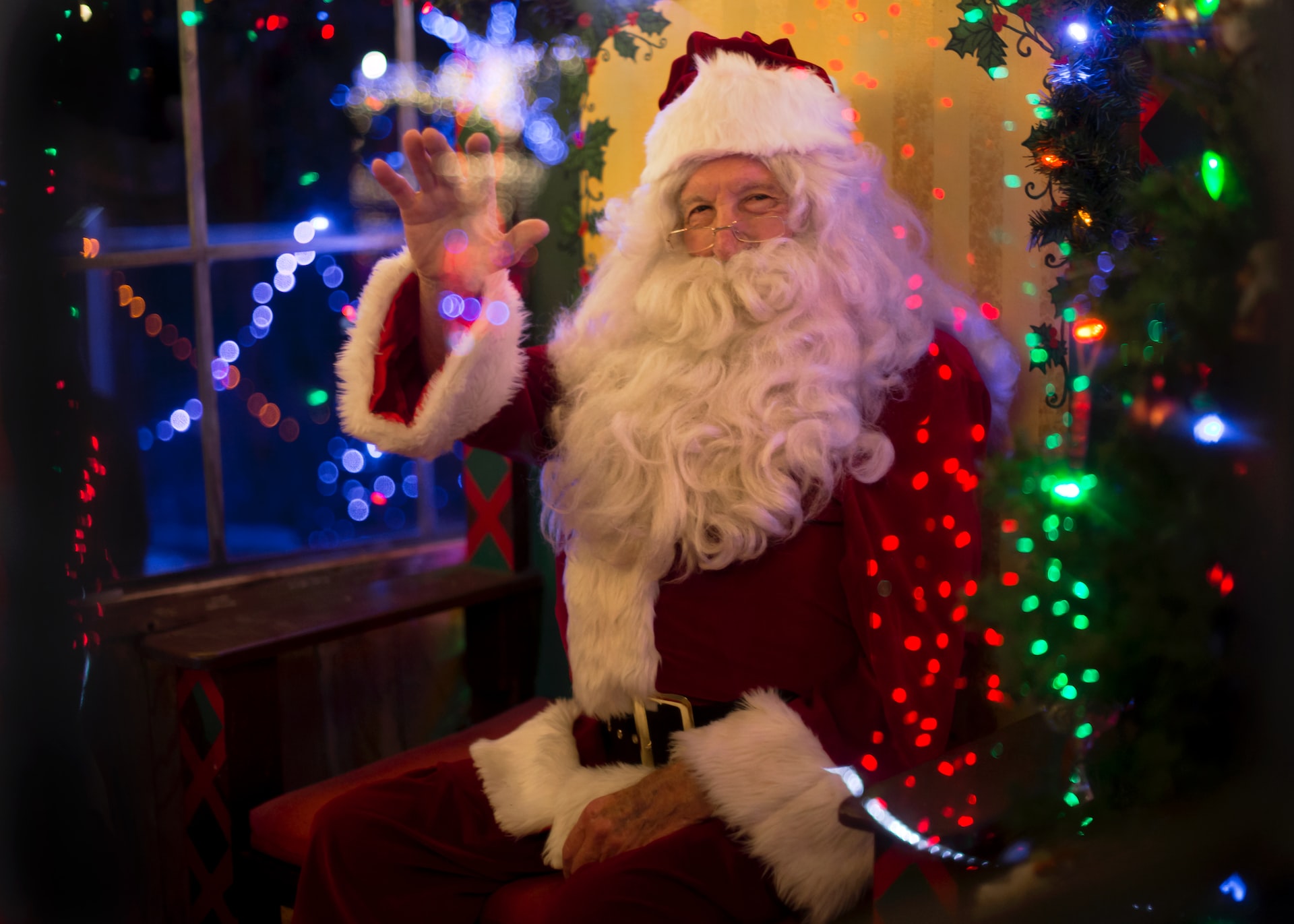 Santa Claus waving in a festive room with colorful lights.