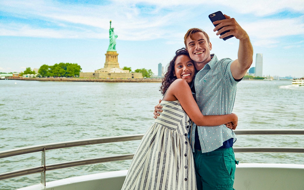 Guests taking a selfie on a boat with the Statue of Liberty in the background.