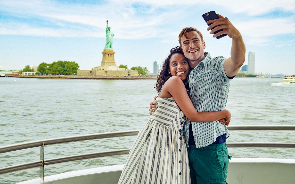 Guests taking a selfie on a boat with the Statue of Liberty in the background.