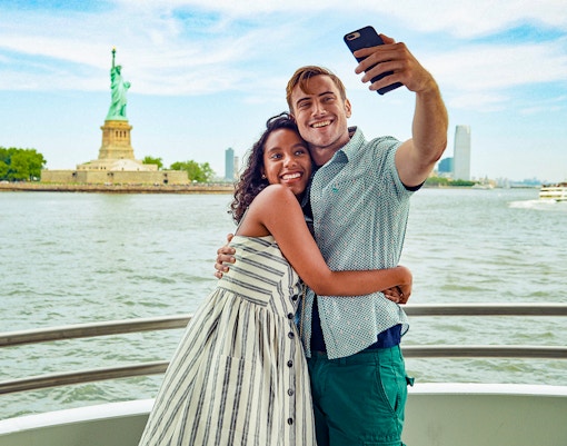 Guests taking a selfie on a boat with the Statue of Liberty in the background.