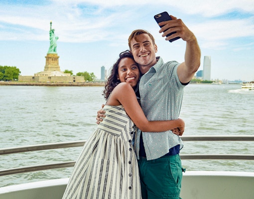 Guests taking a selfie on a boat with the Statue of Liberty in the background.
