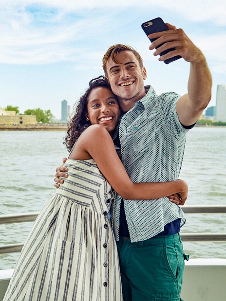 Guests taking a selfie on a boat with the Statue of Liberty in the background.
