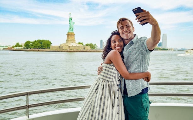 Guests taking a selfie on a boat with the Statue of Liberty in the background.