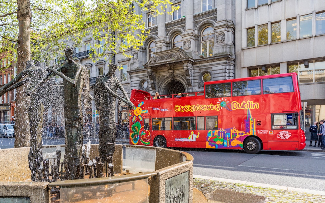 Open-top tour bus passing a fountain in Dublin city center.