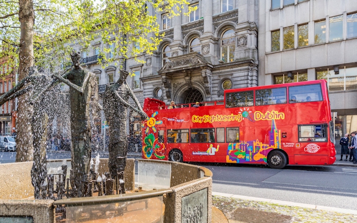 Open-top tour bus passing a fountain in Dublin city center.