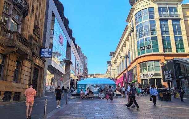 Shoppers walking along Buchanan Street in Glasgow, surrounded by retail stores.