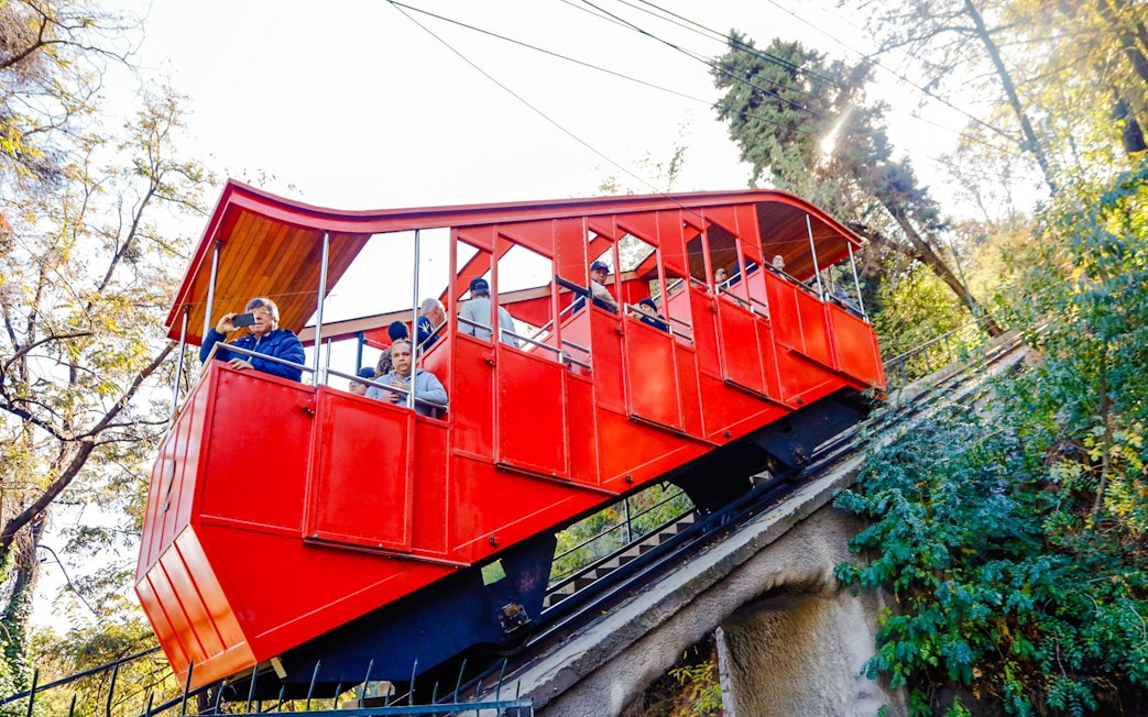 Santiago cable car ascending hillside with passengers.