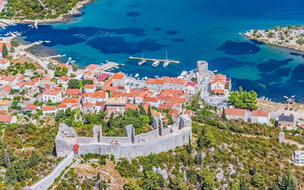 Aerial view of Ston, Croatia, featuring historic walls and red-roofed buildings by the Adriatic Sea.