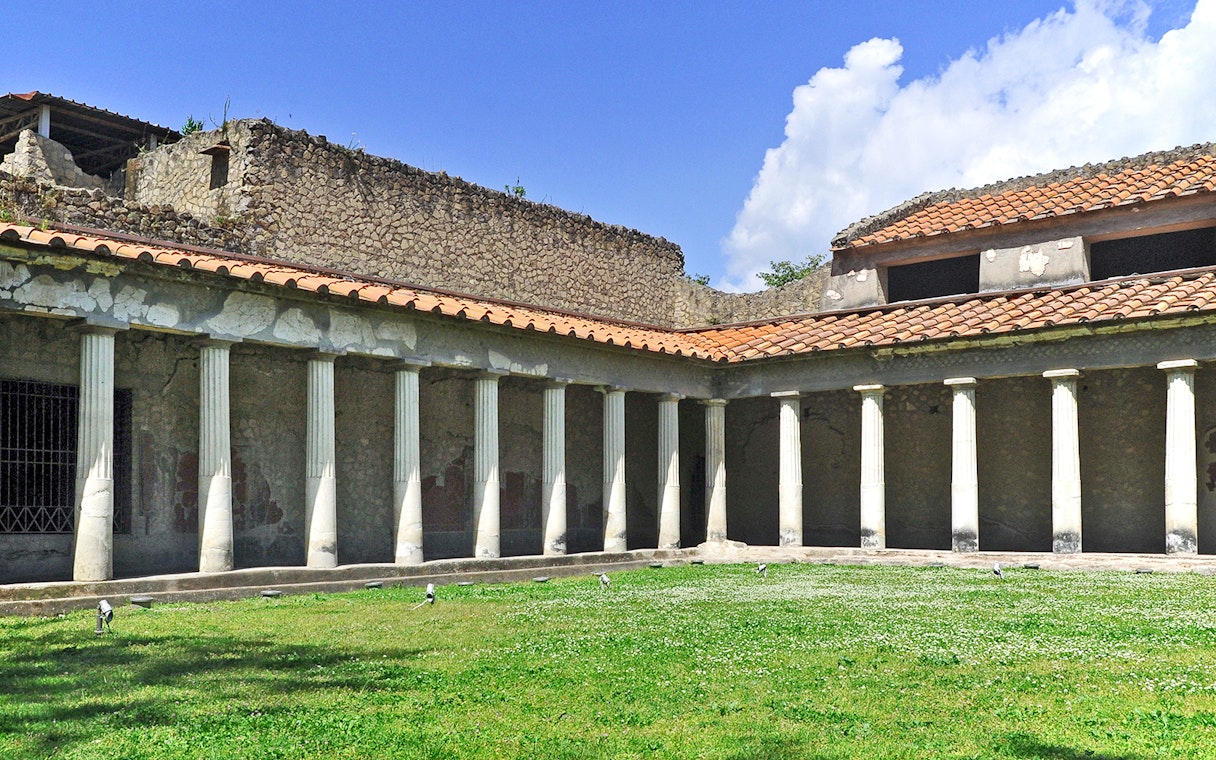 Oplontis villa courtyard with ancient columns and green lawn under blue sky.