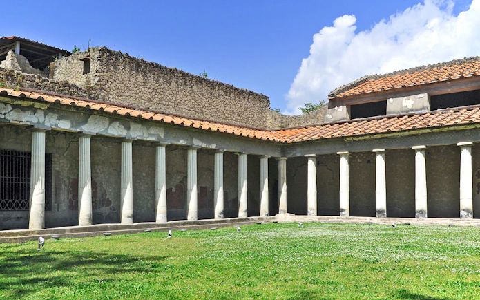 Oplontis villa courtyard with ancient columns and green lawn under blue sky.