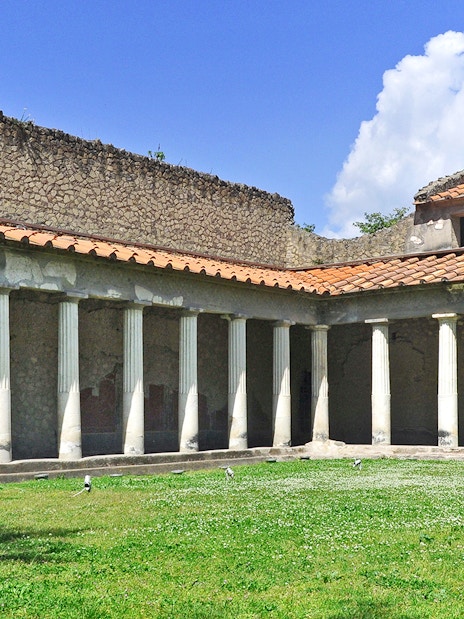 Oplontis villa courtyard with ancient columns and green lawn under blue sky.