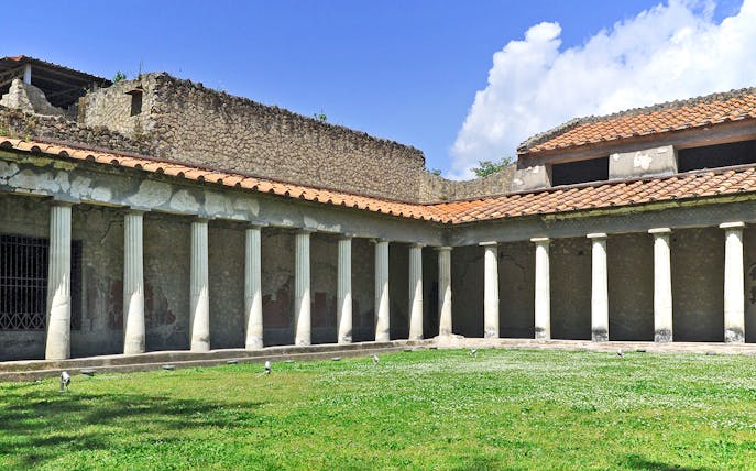 Oplontis villa courtyard with ancient columns and green lawn under blue sky.