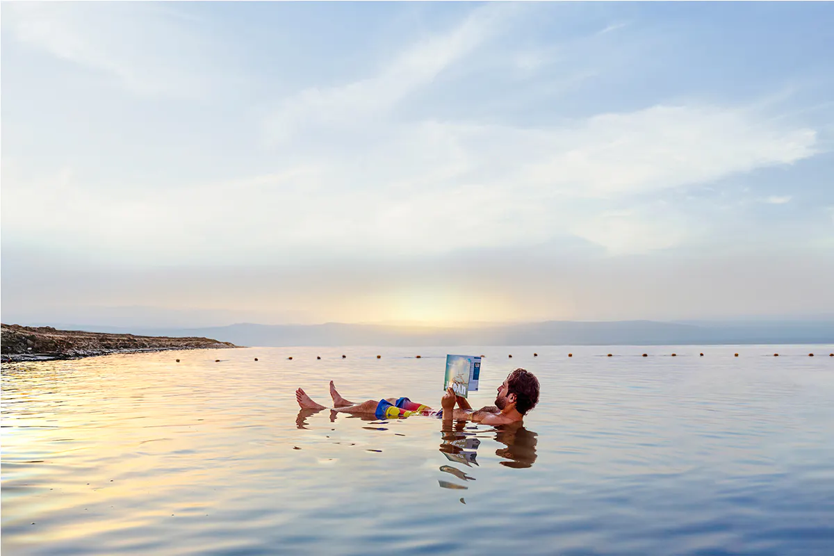 Person floating and reading in the Dead Sea during sunset on a half-day trip from Amman.